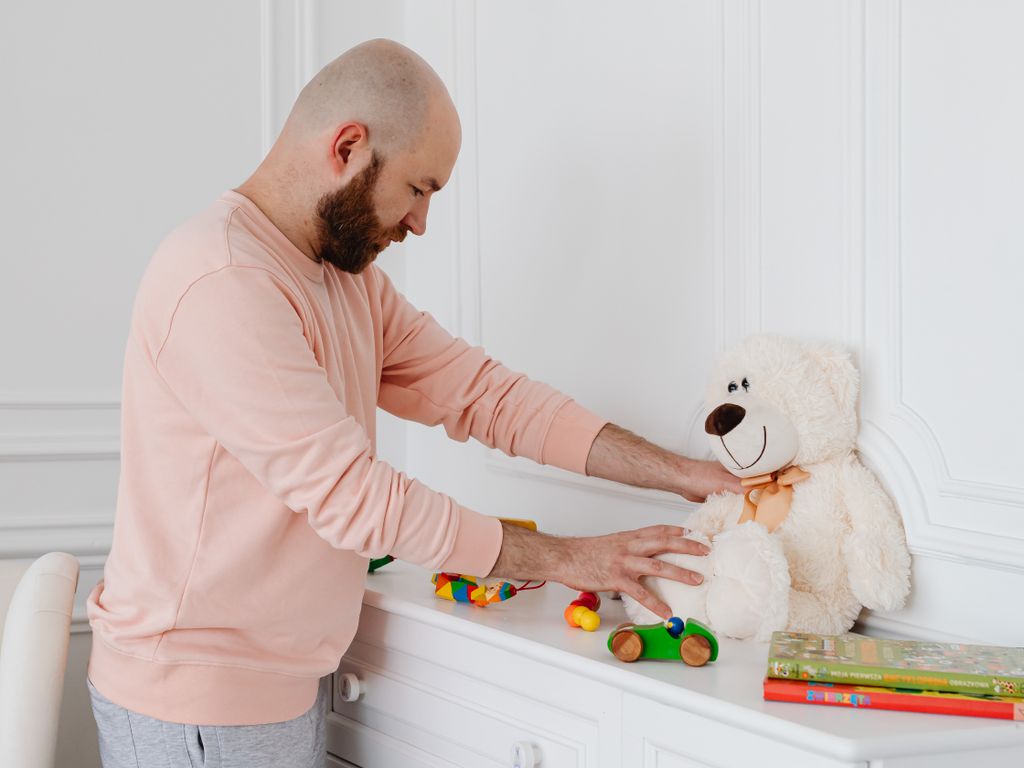 Papa rangeant jouets et peluche sur une commode blanche dans une chambre d'enfant claire