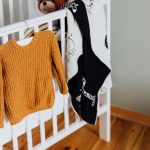 Petit pull moutarde suspendu au bord d’un lit à barreaux blanc