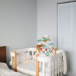 Lit à barreaux blanc et bois avec un mobile coloré, dans une chambre claire
