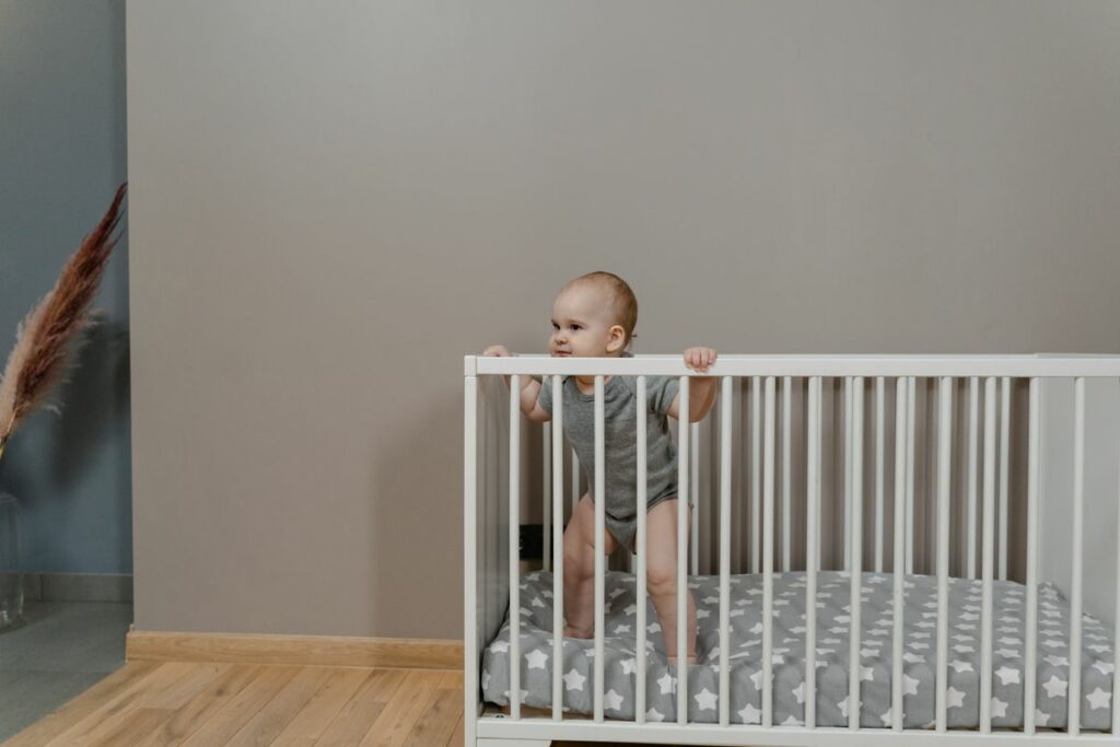 Bébé debout se tenant aux barreaux d'un lit sans tour de lit
