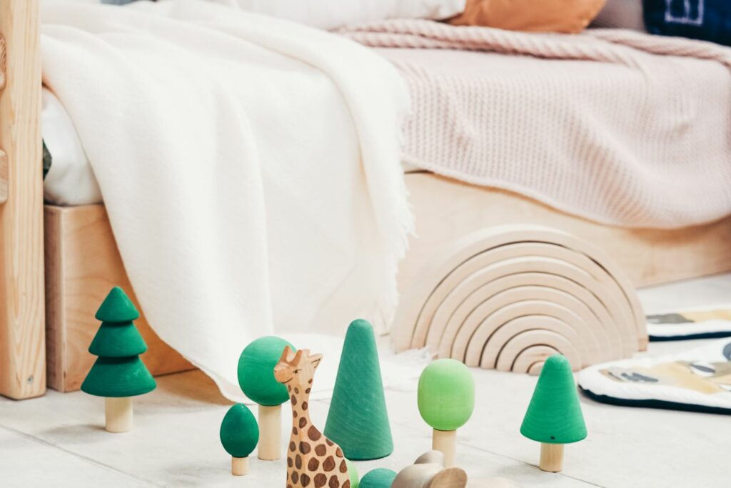 Lit bas avec coussins terracotta et jouets en bois posés au sol dans une chambre de bébé