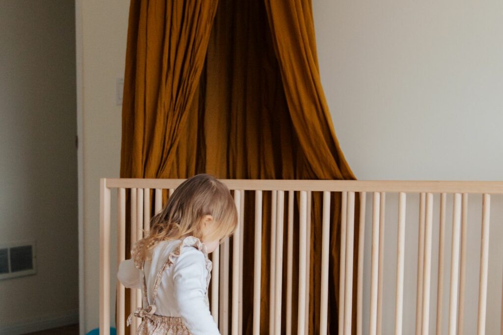Ciel de lit moutarde suspendu au-dessus d'un lit à barreaux en bois, un jeune enfant à côté