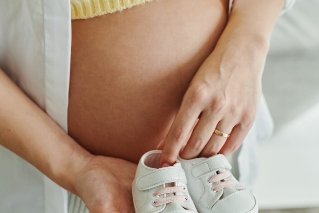Gros plan sur un ventre de femme enceinte tenant de petits chaussons de bébé