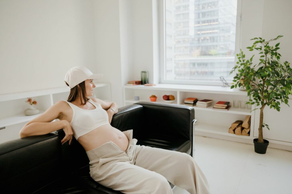 Femme enceinte détendue sur un canapé, regardant par la fenêtre, dans un salon lumineux