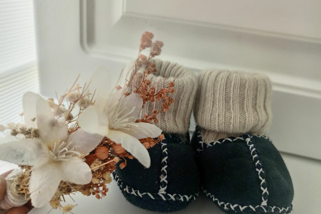 Petits chaussons de bébé posés près de fleurs séchées sur un rebord de fenêtre