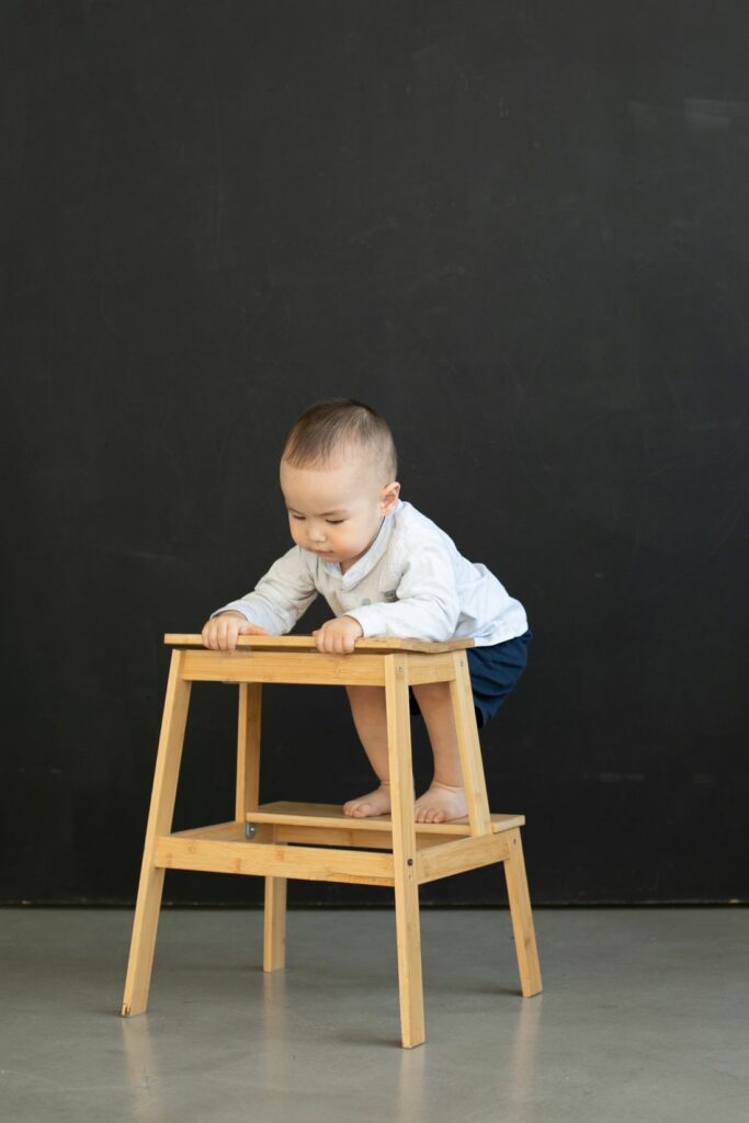 Bébé qui grimpe sur un tabouret en bois, illustrant le risque quand bébé commence à explorer
