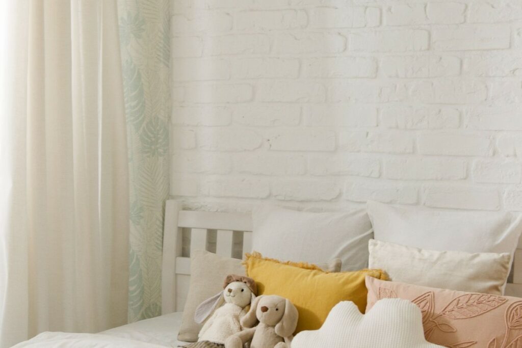 Coin de chambre bébé neutre réchauffé par des coussins moutarde et terracotta