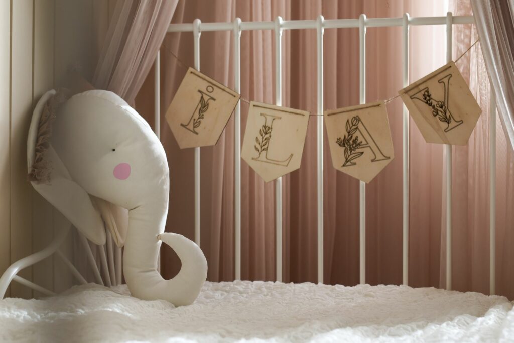 Chambre de bébé fille aux tons vieux rose doux, lit en métal blanc, ciel de lit et guirlande de fanions