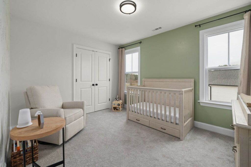 Chambre de bébé mixte aux murs vert sauge, lit en bois clair et fauteuil beige
