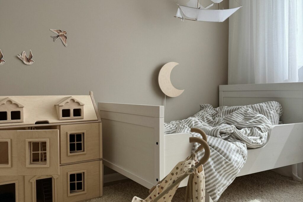 Chambre de bébé aux tons neutres décorée à petit prix : lit simple, maison de poupée en bois, stickers oiseaux, mobile en papier