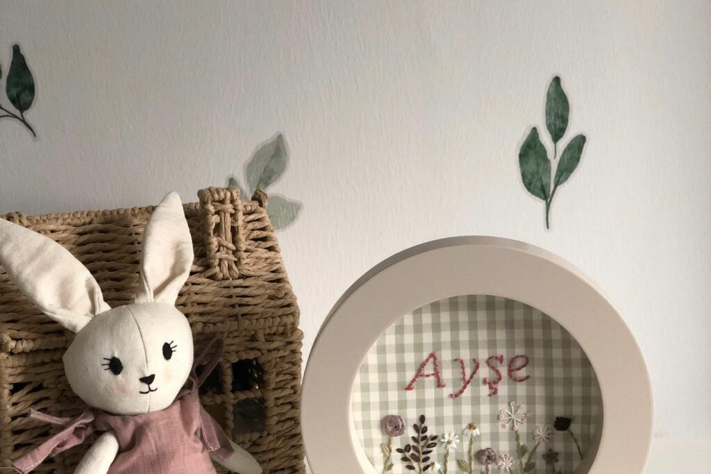 Coin déco d'une chambre de bébé fille : stickers feuillage sauge, lapin en tissu et cadre botanique