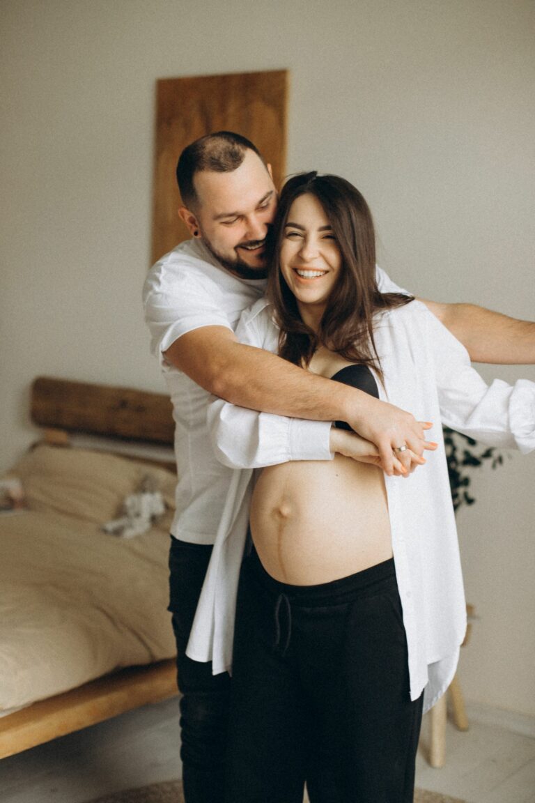 Couple joyeux enlac&eacute;, la future maman riant, dans une chambre lumineuse