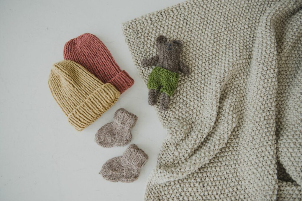 Bonnets, chaussons et doudou en maille sur une couverture crème, essentiels d'une liste de naissance