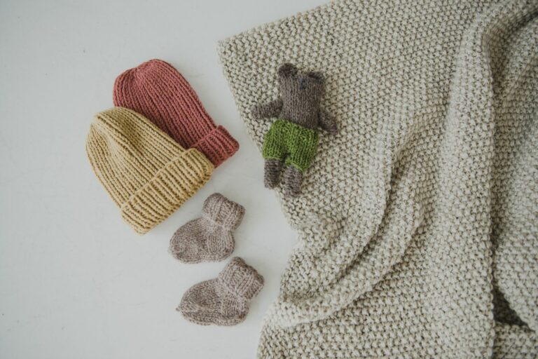 Bonnets, chaussons et doudou en maille sur une couverture crème, essentiels d'une liste de naissance