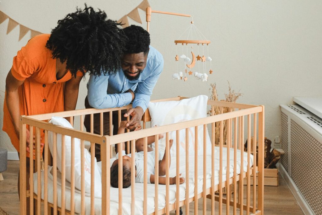 Lit à barreaux en bois naturel, des parents penchés sur leur bébé allongé à l'intérieur