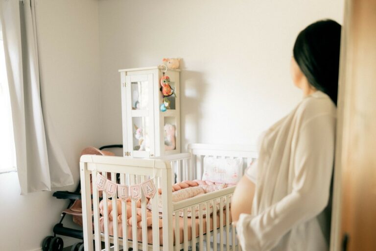 Future maman qui prépare le lit à barreaux dans une chambre de bébé claire et moderne