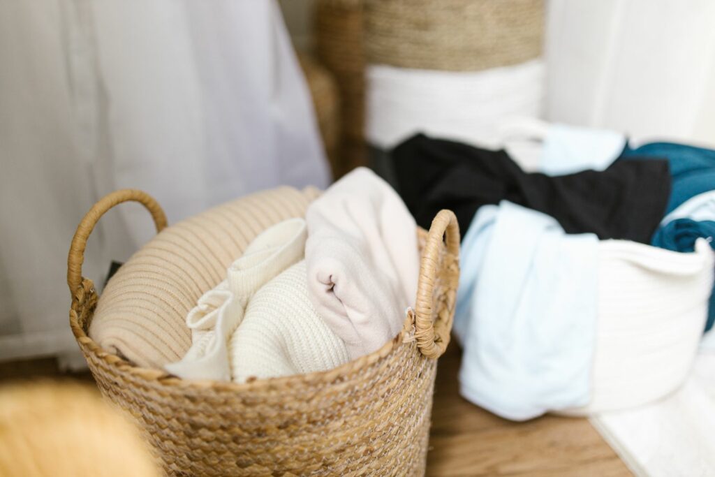 Panier en fibre avec vêtements de bébé pliés et une petite pile à ranger à côté