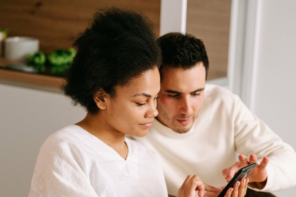 Future maman et son compagnon assis côte à côte, ajoutant des cadeaux à leur liste de naissance sur un téléphone