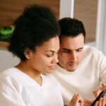 Future maman et son compagnon assis côte à côte, ajoutant des cadeaux à leur liste de naissance sur un téléphone