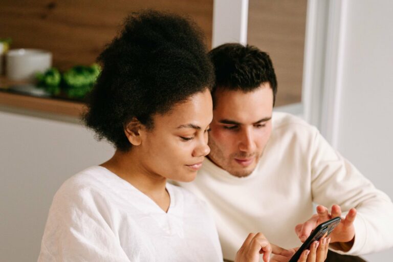 Future maman et son compagnon assis côte à côte, ajoutant des cadeaux à leur liste de naissance sur un téléphone
