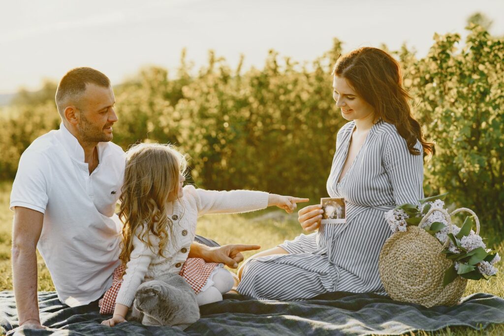 Une petite fille pointe du doigt l'échographie que tient sa maman enceinte, lors d'un pique-nique en famille dans l'herbe