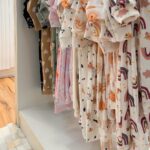 Un portant de petits vêtements de bébé aux imprimés pastel dans une boutique lumineuse