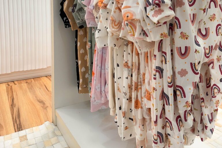 Un portant de petits vêtements de bébé aux imprimés pastel dans une boutique lumineuse