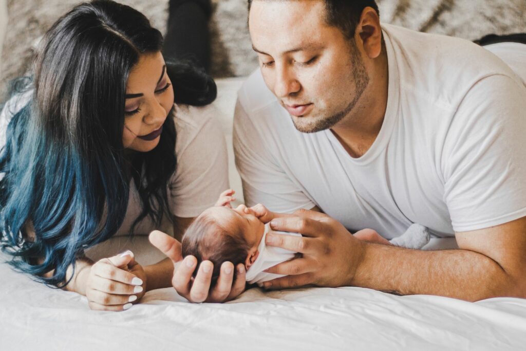 Un couple penché sur son bébé allongé sur un lit clair