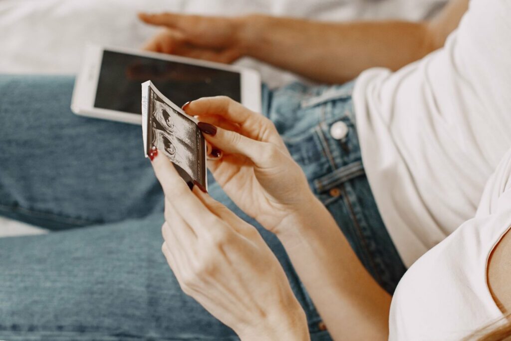 Une future maman tient une photo d'échographie, son téléphone posé sur les genoux