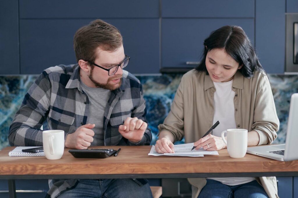 Un couple assis à la table de la cuisine épluche des papiers et fait des calculs