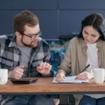 Un couple assis à la table de la cuisine épluche des papiers et fait des calculs