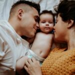 Deux jeunes parents allongés sur un lit embrassent leur nouveau-né
